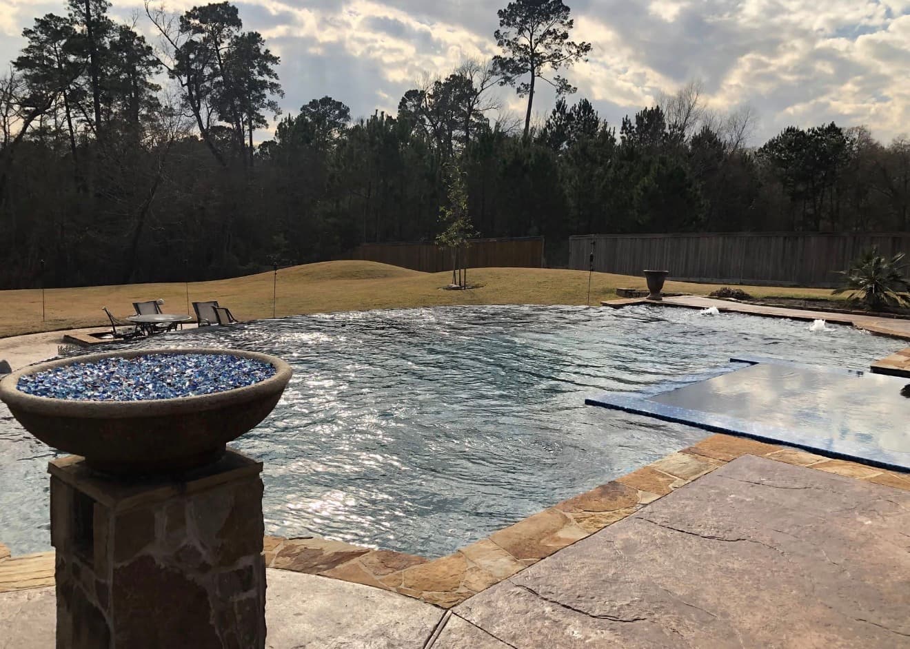 Freeform pool with a submerged tanning ledge, stacked-stone fire bowl, and stamped concrete deck — Houston, TX