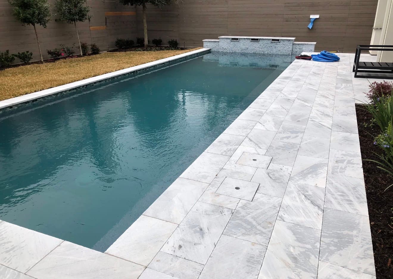 Completed pool with white marble travertine deck, glass tile waterline, and raised fountain — Houston, TX