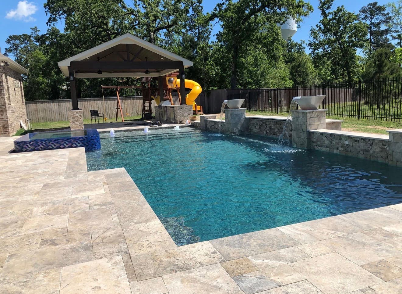 Modern pool with raised stone pillar scuppers, blue glass tile spa, travertine deck, and covered cabana — Houston, TX