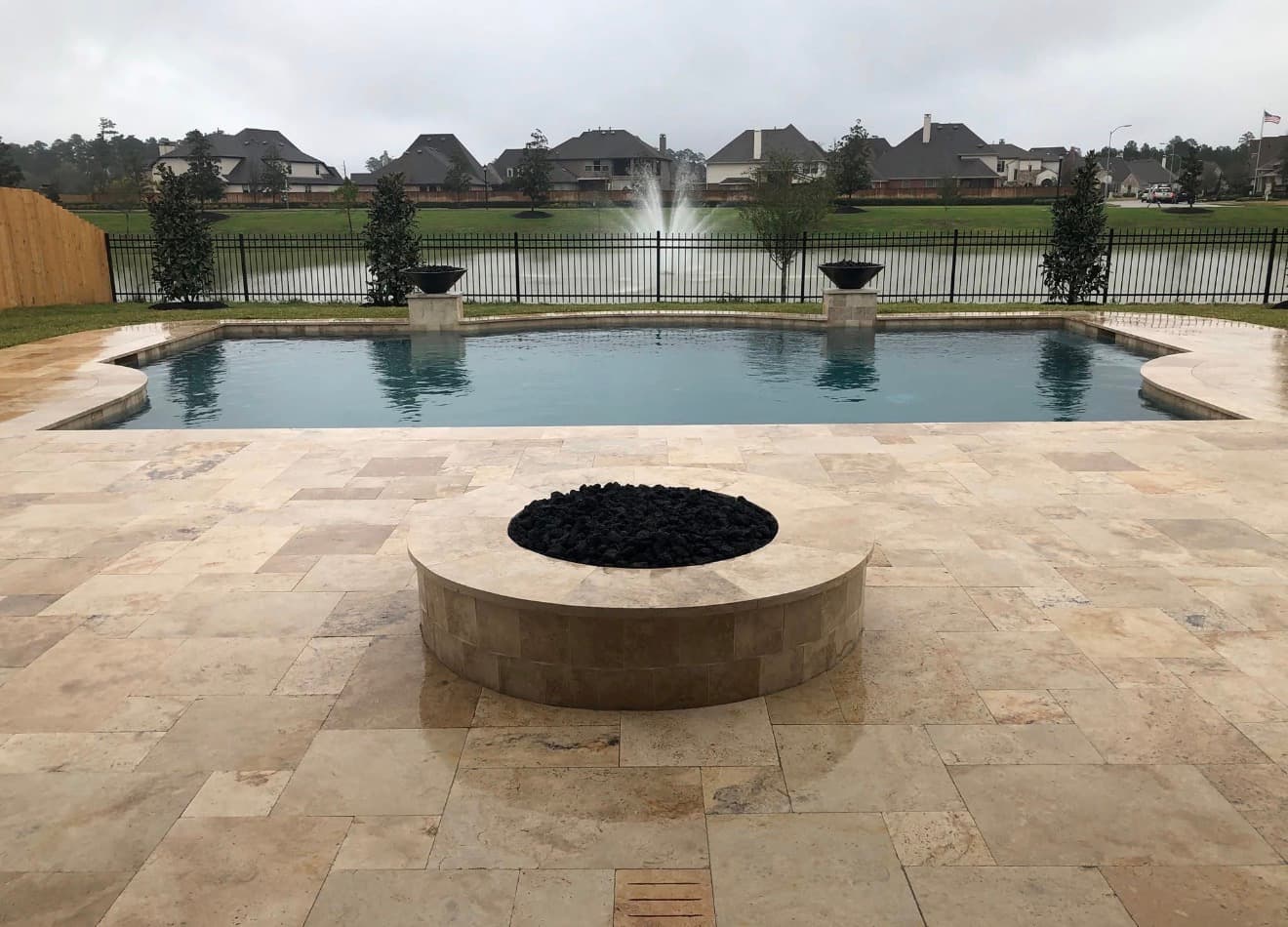 Luxury pool with travertine deck, built-in fire pit, and water fountain feature overlooking a lake — Houston, TX