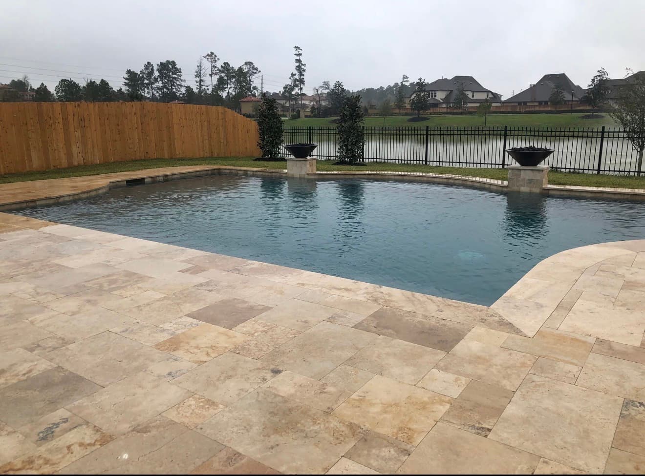 Clean lined pool with full travertine deck, fire bowl pedestals, and lakefront view — Houston, TX